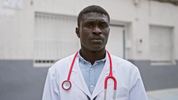 身穿医用白衣和红色听诊器的非洲人自信地站在城市街道上 — 图库视频影像