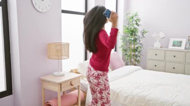 Genç Hintli bir kadın, rahat, şık yatak odasında uzanıp telefonu tutuyor ve günlük rutinlerini anlatıyor..