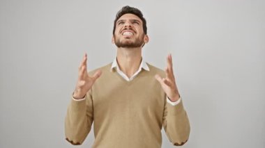 Süveter giymiş genç İspanyol bir adam, izole edilmiş beyaz arka planda sinirli bir ifadeyle bağırıyor, deli ve deli gibi bağırıyor, stres ve öfkeyle kokan kollarını kaldırıyor.