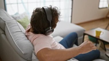 Kulaklıklı, rahat genç bir adamın arka görüntüsü. Kapalı bir koltukta müzik dinliyor.