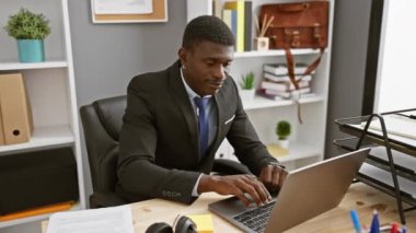Takım elbiseli özgüvenli bir Afro-Amerikan adam modern ofis ortamında masasında çalışıyor ve dans ediyor..