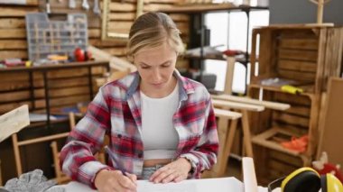 Kafası karışmış, budala bir ifade, genç sarışın marangoz kadın marangozluk masasından şüphe ediyor, güzel ve kapalı atölyede kafası karışmış.