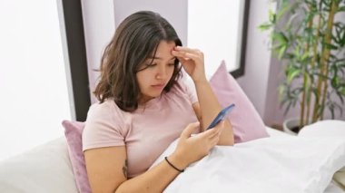 Endişeli bir İspanyol kadın yatak odasında akıllı telefonundan bir mesaj okuyor. Bağlılık ve gizlilik sorunlarını sembolize ediyor..