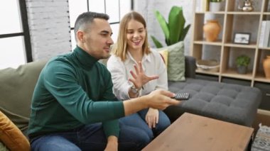 Neşeli bir adam ve kadın, rahat bir anı rahat bir oturma odasında uzaktan kumandayla paylaşıyorlar..