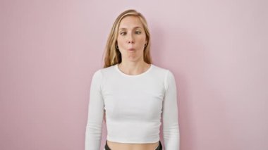 Çılgın sarışın kadın balık suratlı bir ifadeyle, izole edilmiş pembe arka planda komik bir jest yapıyor. Kendinden emin, dudakları büzüşmüş genç bir kadının neşeli portresi..