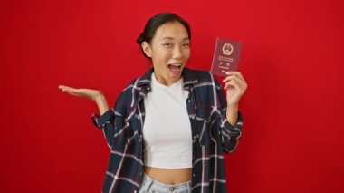 Neşeli genç Çinli kadın pasaport gösteriyor, zaferi neşeli bir gülümsemeyle kutluyor, izole edilmiş kırmızı arka planda neşeli bir ifade var.