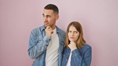 Endişeli aşk, kot gömlekli güzel bir çift, el pençe divan duran, pembe izole bir arka plan üzerinde endişeli bir soru üzerinde kafa yoran gergin.