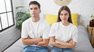 Genç bir çift, minimalist yatak odalarında yan yana otururken ilişki sorunlarını dile getirirken gerginlik sergiliyor..