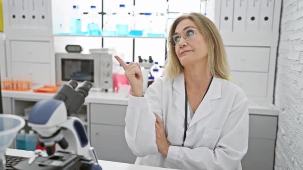 Lächelnde Blondine Wissenschaftlerin Mittleren Alters Fröhlich Auf Die Seite Zeigend — Stockvideo
