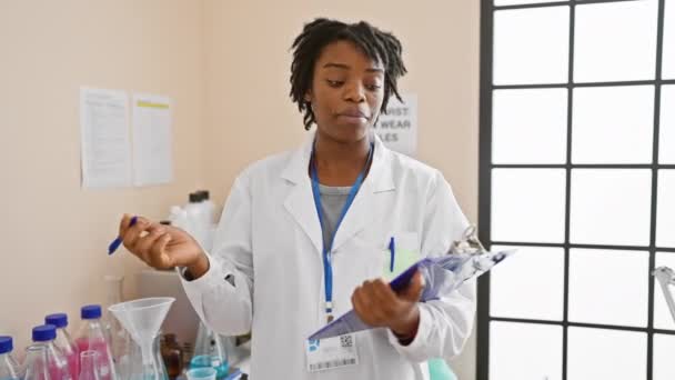 実験室で働くドレッドロックを持つ若いアフリカ系アメリカ人女性 ノートを取り テストチューブを保持 — ストック動画