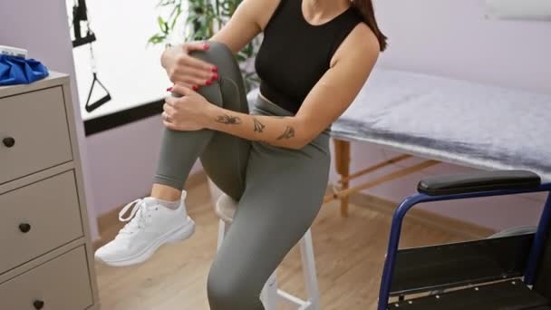 タトゥーを持つ若い女性は 医療リハビリテーションクリニックで膝を抱え 怪我や治療の可能性を示しています — ストック動画