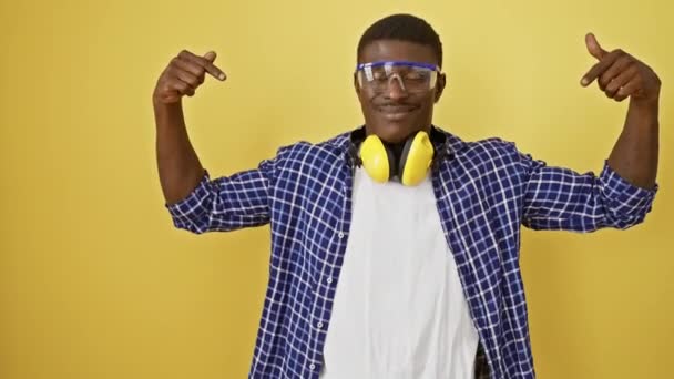 安全眼鏡のアフリカ系アメリカ人男性は 黄色の背景を誇らしげに指摘しています 幸せで自信に満ちた 成功の有望な例です — ストック動画