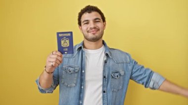 Emirlik pasaportu taşıyan genç Arap adam gülümsüyor mutlu bir şekilde el pençe divan duran sarı arka planda el pençe divan duruyor.