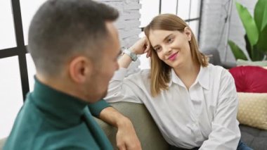 Bir kadın ve bir erkek, modern bir oturma odasında yakın otururlar, bir anlık yakınlık ve bağlantının tadını çıkarırlar..