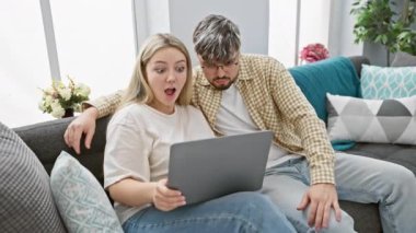 Neşeli genç bir kadın ve erkek, samimi bir oturma odasında, ilişki başarısını simgeleyen dizüstü bilgisayarla bir beşlik çakarak kutluyor..