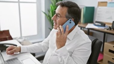 Modern ofis ortamında akıllı telefon kullanan gözlüklü olgun bir işadamı.