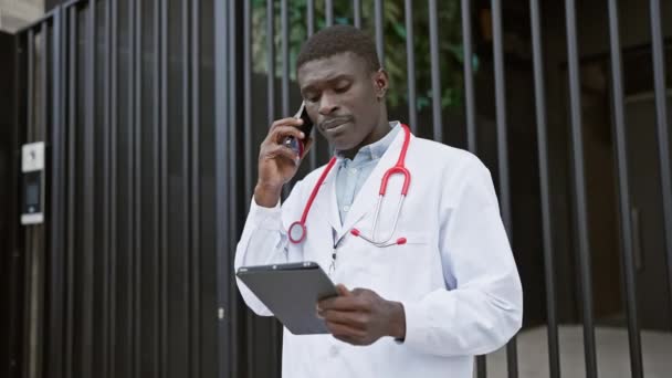 在城市的医院外 非洲男医生用平板电脑和智能手机交谈 — 图库视频影像