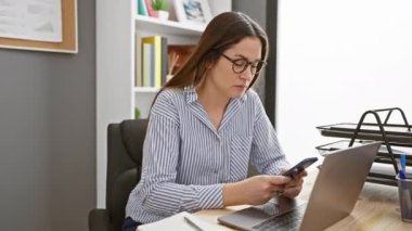 Bilgisayarı, akıllı telefonu ve not defteriyle ofis masasında çalışan odaklanmış bir kadın.