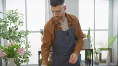 Gözlük takan sakallı bir adam çiçekçi dükkanında çiçek düzenliyor..