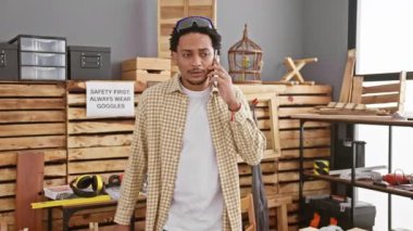 Marangozluk atölyesinde ahşap ve aletlerle telefonda kıvırcık saçlı yakışıklı bir adam..