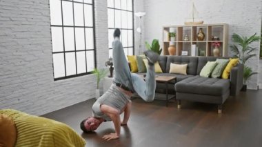 Genç bir adam modern bir salonda tökezliyor ve düşüyor. Evdeki sakarlığı ya da kazayı ifade ediyor..