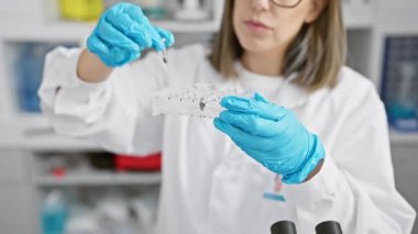 Odaklanmış İspanyol kadın laboratuvar ortamında araştırma yapıyor, test tüplerini dikkatlice inceliyor..