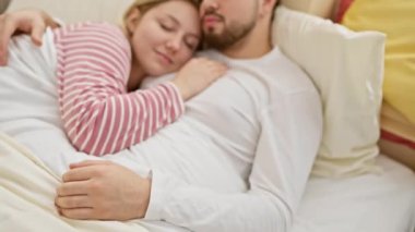 Sevecen bir çift, rahat, aydınlık bir yatak odasında, beyaz yatak örtüsü ve renkli yastıklarla birlikte uyur.