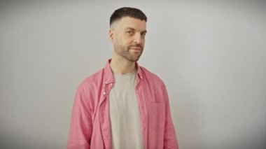 Tişörtlü neşeli, genç İspanyol adam, izole edilmiş beyaz duvarın karşısında duruyor, kendine güvenerek gülümsüyor ve işaret parmağıyla işaret veriyor. Mükemmel ifadesiyle pozitiflik ve serinlik yayar..