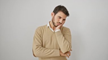 Genç, sakallı, sıkıntılı ve stresli bir İspanyol 'un portresi. Ayakta duruyor, kolları çapraz, süveter giyiyor. Yorgun görünüyor, depresyon sorunlarını beyaz, soyutlanmış bir arka planda düşünüyor..