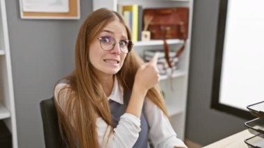 Ofisteki genç sarışın iş kadını, işaret parmağıyla işaret ediyor! Endişeli yüz ifadesi, gergin bakışlar. Sürpriz! İş yerinde endişeli, kapalı alanda dram yaşanıyor.