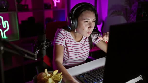 专注的女人晚上穿着耳机和麦克风在一间五颜六色的照明房间里玩游戏 — 图库视频影像
