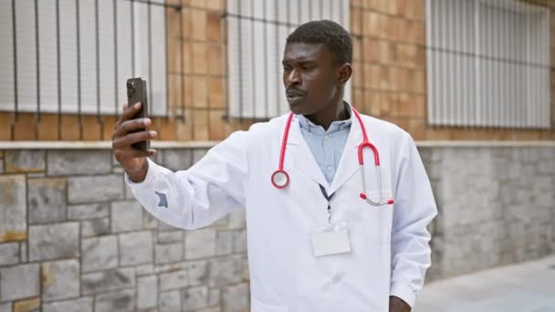 非洲裔美国医生带着智能手机 穿着实验室外套和听诊器 走在室外 — 图库视频影像