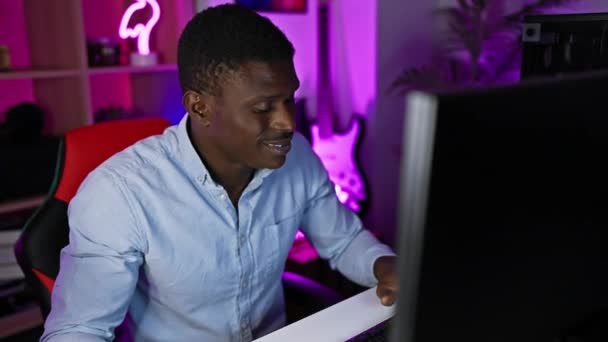 非洲男人晚上在霓虹灯下的游戏室里与电脑一起工作时表现出喜悦 — 图库视频影像
