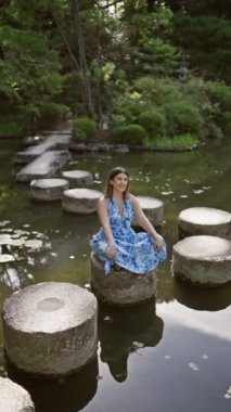 Güzel bir İspanyol kadın taştan bir yolda oturuyor, doğanın yeşil yaz ihtişamını alıyor, Heian Jingu, Kyoto 'da sakin bir göl kenarında - ilahi bir yolculuk, geleneksel Japon tapınağına bakıyor.