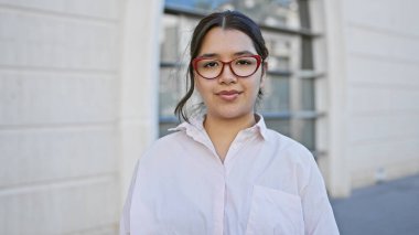 Gözlüklü İspanyol kadın bulanık bir sokak geçmişine karşı güvenle poz veriyor, kameraya bakıyor..