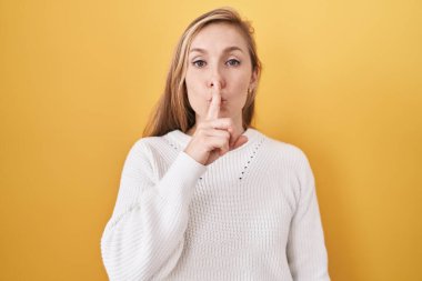 Sarı arka planda beyaz süveter giyen beyaz bir kadın sessiz olmak istiyor. sessizlik ve gizli konsept. 
