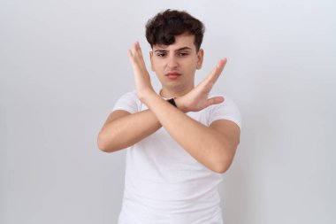 Gündelik beyaz tişört giyen genç adam reddedilme ifadesi kollarını kavuşturarak negatif işaret veriyor, kızgın yüz ifadesi takınıyor 