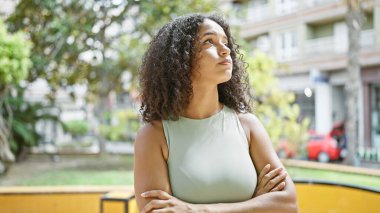 Dinamik, genç İspanyol bir kadın, havalı yaşam tarzı titreşimleri yayıyor. Konsantrasyonuna dalmış, kollarını kavuşturup güneşli bir parkta duruyor. Rahatlamış ama ciddi modanın mükemmel bir ifadesi.