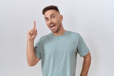 Hispanic man with beard standing over white background pointing finger up with successful idea. exited and happy. number one. 