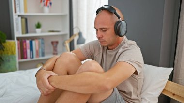Young hispanic man listening to music relaxed on bed at bedroom