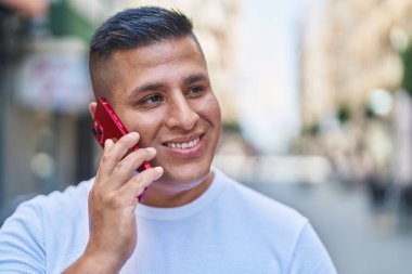 Genç Latin adam gülümsüyor. Kendine güveniyor. Akıllı telefondan konuşuyor.