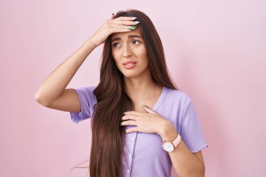 Uzun saçlı genç İspanyol kadın pembe arka planda duruyor. Hastalık, ateş, grip ve virüs için alnına dokunuyor. 