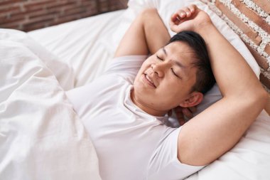 Young chinese man lying on bed sleeping at bedroom