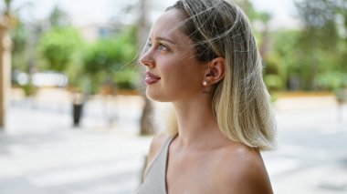 Sokakta ciddi bir ifadeyle yan tarafa bakan genç sarışın kadın.