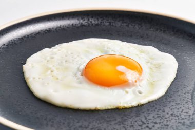 Koyu yapışkan bir tavada parlak sarısı olan tek bir sahanda yumurtanın yakın çekimi kahvaltıyı ve sağlıklı beslenmeyi betimliyor..
