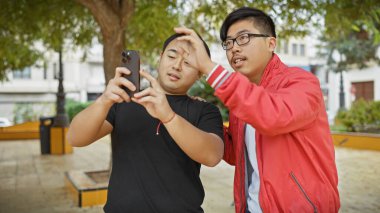 Şehir caddesinde akıllı telefon kullanan iki Asyalı adam ekrana yakından bakıyor..
