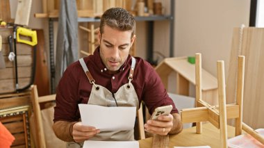 Odaklanmış bir İspanyol ahşap atölyesinde telefon tutarken belgeleri inceliyor..
