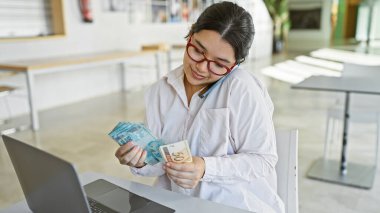 Genç bir İspanyol kadın, Brezilya para birimini modern ofis ortamında inceleyerek finansal çalışmalarını yansıtıyor..