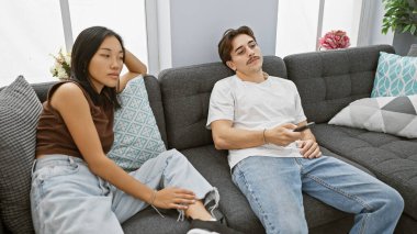 Modern bir oturma odasında uzanan ırklar arası bir çift. Kadın dinleniyor ve adam uzaktan kumanda tutuyor..