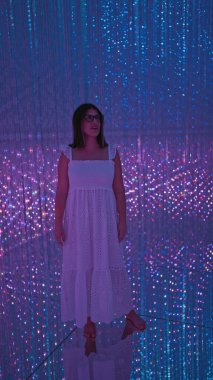 Işıl ışıl İspanyol kadın, gözlüklü güzel, modern müzedeki fütürist bir ışık sergisine daldırıyor, modern teknoloji ve yaratıcılığın floresan neon gösterimiyle yıkanıyor..